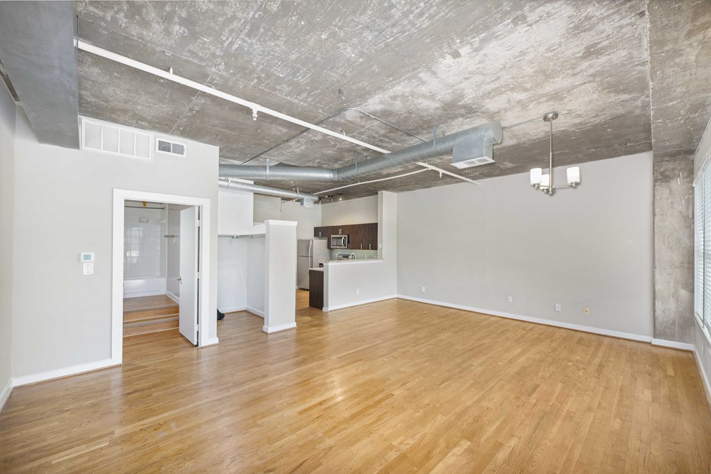 an empty living room with a wood floor and a ceiling with exposed ducts